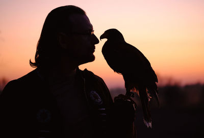 Silhouette of man and wild bird over sunset sky looking on each other buzzard or eagle symbol of