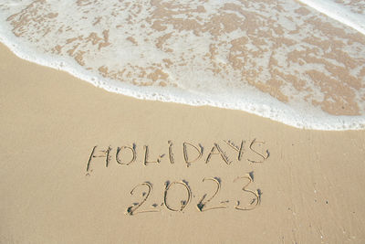 Holidays 2023 lettering on the beach with wave and clear blue sea.