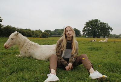 Portrait of woman sitting on field against sky