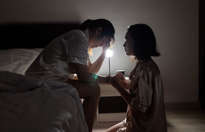 Side view of man holding mobile phone while sitting on bed