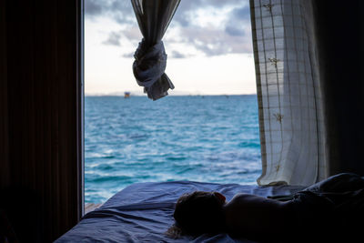 Girl sleeping on bed by sea against sky