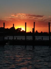 Silhouette wooden posts in river against sky during sunset