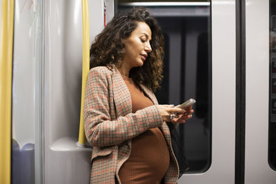Pregnant female entrepreneur using smart phone while traveling by train