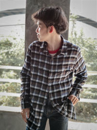 Young man looking away while standing against window