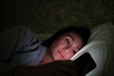 Mid adult woman using mobile phone while lying on bed in darkroom