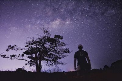 Silhouette man standing by tree against sky at night