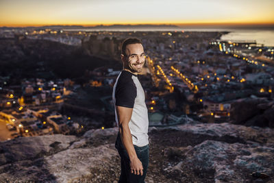 Full length of woman standing by cityscape against sky during sunset