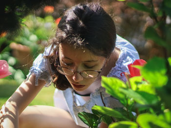 A caucasian teenager girl in glasses enthusiastically looks for chocolate easter eggs in bushes