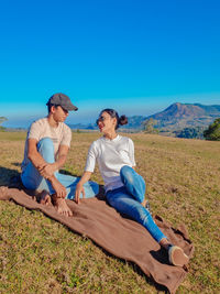 Full length of couple sitting on land against blue sky