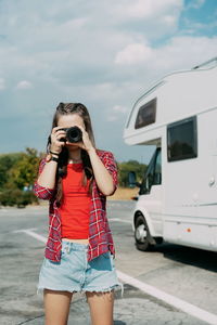 Woman photographing by camera while standing against sky