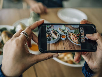 Midsection of man photographing with mobile phone on table