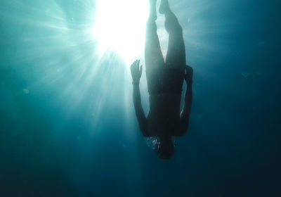 Silhouette of a man in the rays of the sun floats in the black sea