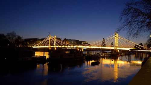 Illuminated bridge over river against clear blue sky at night