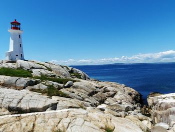 Lighthouse by sea against clear blue sky