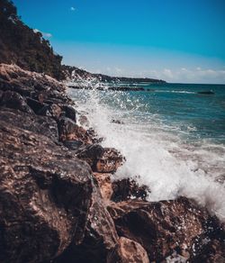 Waves splashing on rocks at shore against sky