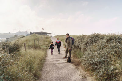 Father with two daughters walking on road against sky