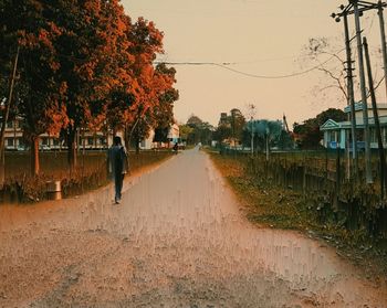 Man walking on road by canal against sky during sunset