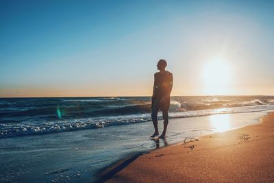 Silhouette mature man standing at beach against clear sky during sunset