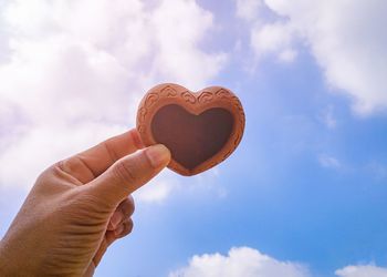 Close-up of hand holding heart shape against sky