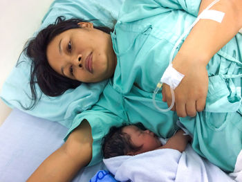 High angle view of newborn baby with mother lying on bed in hospital