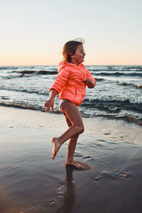 Playful little girl enjoying a free time over sea on a sand beach at sunset during summer vacation