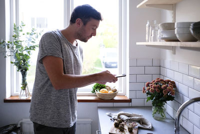 Mid adult man photographing food through smart phone at kitchen counter