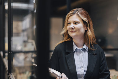 Smiling businesswoman looking away while standing at office