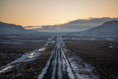 Empty dirt road along landscape against sky during sunset