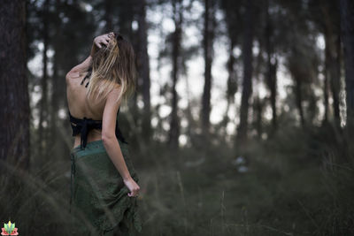 Young woman standing by tree in forest