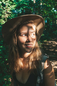 Close-up of smiling young woman in hat looking away in forest