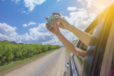 Man driving car on road amidst field against sky