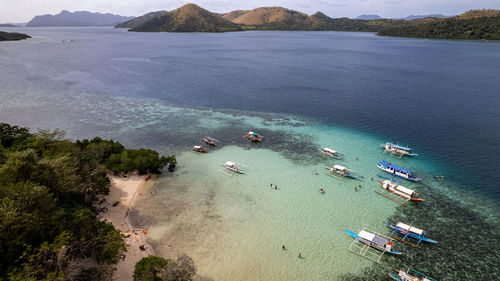 In the photo, a vibrant tropical boat near a beautiful beach or rocky shore.