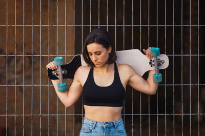 Woman with skateboard standing by fence