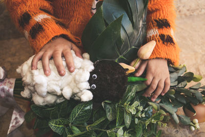 Midsection of person holding toy and leaves bouquet while sitting outdoors