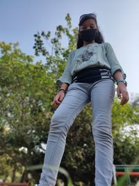 Low angle view of girl wearing mask standing against trees