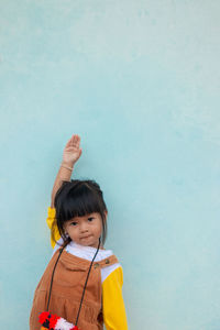 Portrait of cute baby girl with hand raised standing against wall