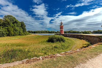 Lighthouse on field by building against sky