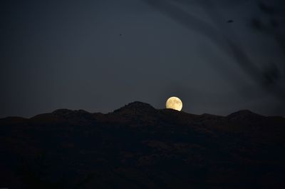 Low angle view of moon in mountains against sky