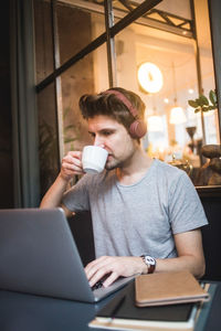 Confident businessman drinking coffee while using laptop at desk in office