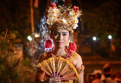 Portrait of young woman looking at illuminated camera at night