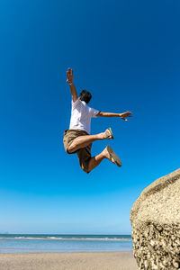 Low angle view of man jumping on beach against clear sky