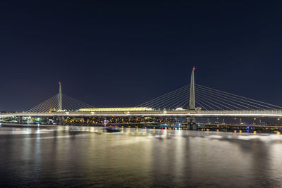 Illuminated bridge over river against sky at night