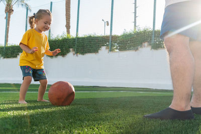 Cute little girl in yellow t-shirt going to kick the ball to father