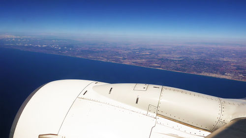 Aerial view of airplane wing over landscape against blue sky