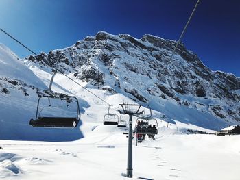 Ski lift over snowcapped mountains against clear blue sky