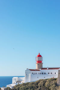 Lighthouse by sea against clear sky