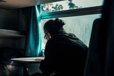 Rear view of woman looking through window at home