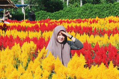 Portrait of smiling young woman standing by yellow flowering plants