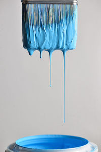 Close-up of blue paint dripping into container against wall