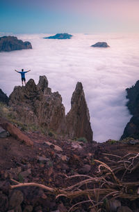 Man standing on rocks by sea against sky